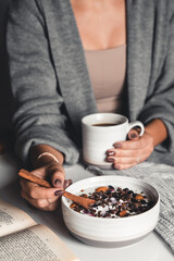 A young girl drinks morning coffee, eats a healthy breakfast and reads a book. Morning routine. Stylish manicure. Correct habits. Holding a cup in his hands - 474200209