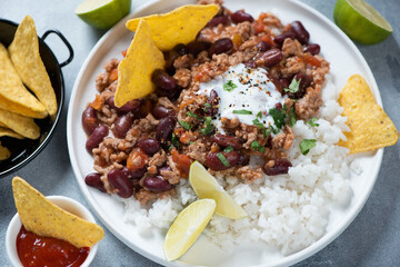 Closeup of tex-mex chili con carne or spicy meat stew served with rice and nachos on a white plate, studio shot