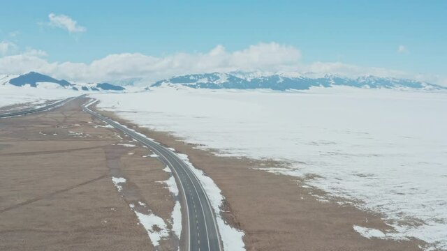Aerial view of empty road along snowy alpine mountains and open land. Miles and miles of empty open land with no people.