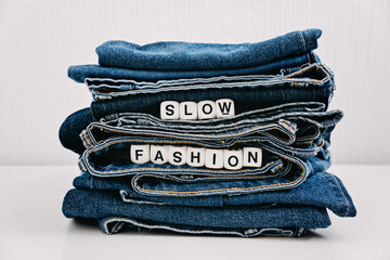 Slow fashion, second hand, Vintage Shopping, slow fashion, Sustainable fashion concept. Stack of blue old denim jeans with the words slow fashion - obrazy, fototapety, plakaty