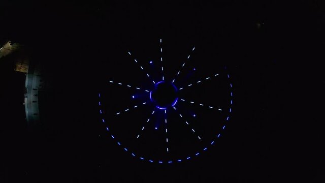 Aerial descending drone footage of an abstract, colourful stroboscopic circle led lights show placed in a fountain in Bratislava, Slovakia. The lights are pulsating  in form of a star and a circle