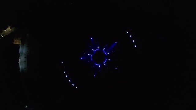 Aerial descending drone footage of an abstract and colourful circle led lights show placed in a fountain in Bratislava, Slovakia. The lights are pulsating and are in form of a star and a circle.