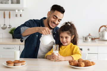 Obraz na płótnie Canvas Happy Arab Dad And Daughter Eating Pastry And Drinking Milk In Kitchen