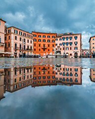 Buildings surrounding Piazza Navona and the Fontana di Nettuno reflected on a water puddle in the morning