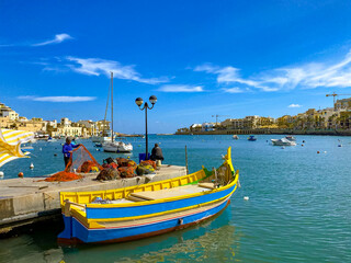 Naklejka na ściany i meble Bright colored boat and fishermen with nets in the port on the island of Malta