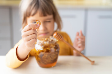 Child girl eating golden honeycomb and beeswax in a jar of honey on the table. Fresh organic honey...