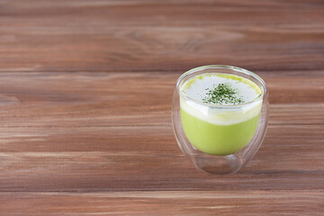 Matcha latte tea with coconut milk in a glass on a brown wooden table. Horizontal orientation, copy space.