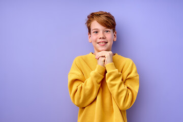 Dreaming. young redhead Caucasian child boy isolated on purple studio background. Portrait. Concept of human emotion, facial expression, beauty, childhood. Copy space for advertisement.