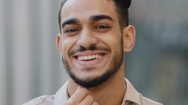 Extreme close-up male portrait outdoors face of bearded hispanic arabic guy brunette man client of barbershop satisfied happiness smiling touching chin beard enjoying haircut after shaving service
