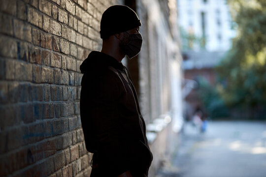 afro american man in black mask standing at street waiting for victim to commit a crime. Black african guy in hat and black wear. cruel man outdoors. Concept portrait of dangerous criminal