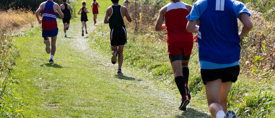 Rear vie of boys running on a grass field during a 5K cross country race