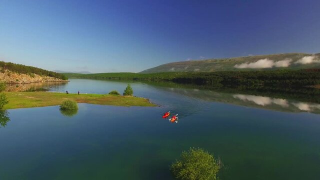 Drone is moving up and tilting down. Twa kayaks slowly moving away from camera to big dam in distance