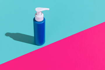 One blue pump bottle for cosmetics product, cream, lotion without logos standing isolated over magenta blue background.