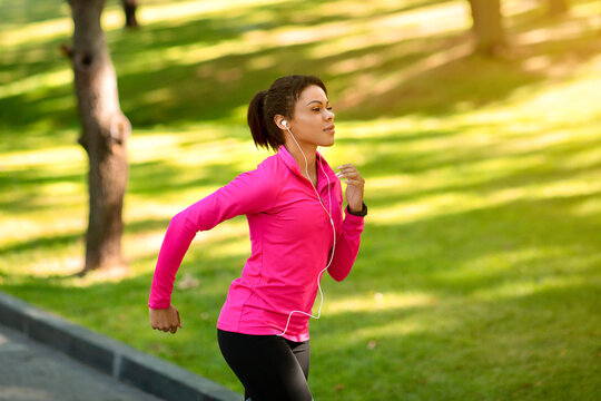 Side view of athletic black woman running by park