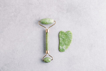 Green jade stone and gua sha massage roller for natural lifting on grey stone background....