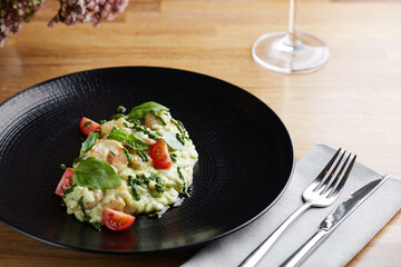 risotto with pesto, basil and cherry tomatoes closeup in black plate on wooden table. risotto on wooden table restaurant