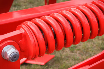 Big and hard red steel spring as part and detail of industrial or agricultural machine