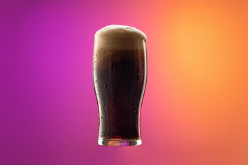 One full glass of frothy dark beer isolated over gradient purple and orange color background in...