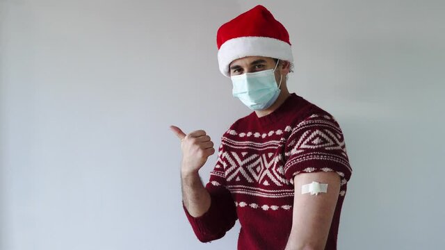 Covid safe christmas. Man with santa hat and mask points away with thumb