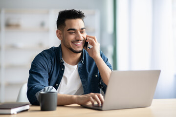 Successful middle-eastern guy talking on phone while working at home