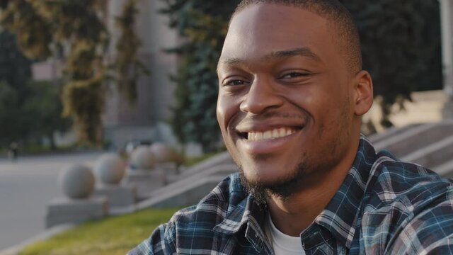 Portrait african american happy carefree cheerful smiling man guy looking into distance thinking turns to camera with toothy smile posing outdoors in city, close-up head satisfied glad male face