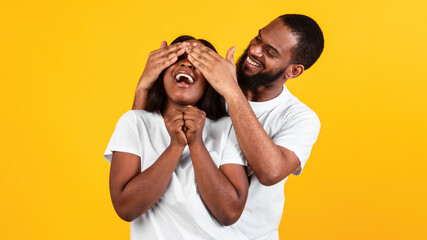 Happy black man making surprise for his woman, covering eyes