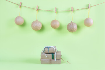 Five craft Christmas balls on the rope with pegs and three presents in the craft paper on the green background. Christmas or New Year beige and green banner.