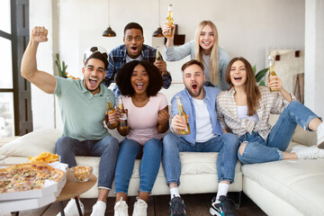 Group of young friends with snacks and beer watching football game on television, cheering for...