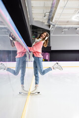 full length of amazed woman in white scarf, sweater and ear muffs posing on ice rink.