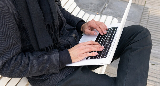 Anonymous male female entrepreneur sitting on bench and working on laptop on street