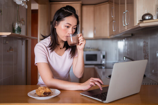 Asian Woman With Beverage Browsing Laptop