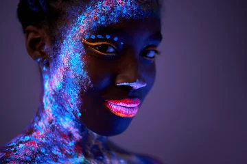 Schwarze Frau mit Körperkunst, die im ultravioletten Licht leuchtet. schöne Frau in fluoreszierendem Pulver gemalt. isolierter dunkelvioletter Raum. Schönheit, Modekonzept. ungewöhnliches Shooting © alfa27