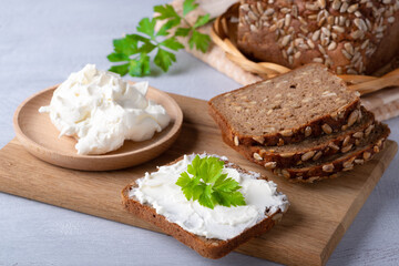 Home made rye bread on a wooden cutting board with curd cheese, ricotta and herbs
