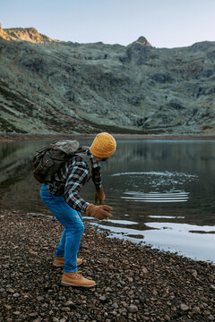 Unrecognizable traveler skimming stone on water surface