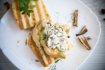 fried bread toast with cheese spread with boiled dried mushrooms on a wooden table.