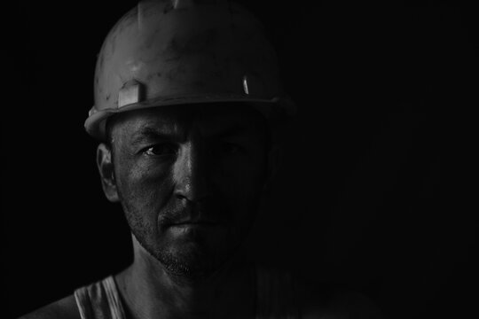 Portrait miner in helmet and undershirt with dirty face.