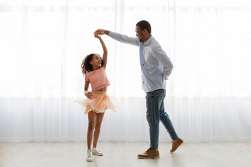 Black father and daughter dancing at home, full length shot