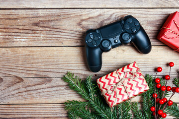Joystick gaming controller with gift box, fir brabch and red berries on wooden background. Xmas...
