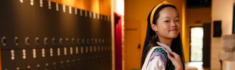 Asian girl smiling while standing with backpack at school