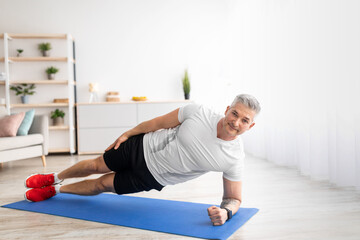 Healthy lifestyle concept. Fit mature man standing in side plank on sports mat at home, exercising in living room