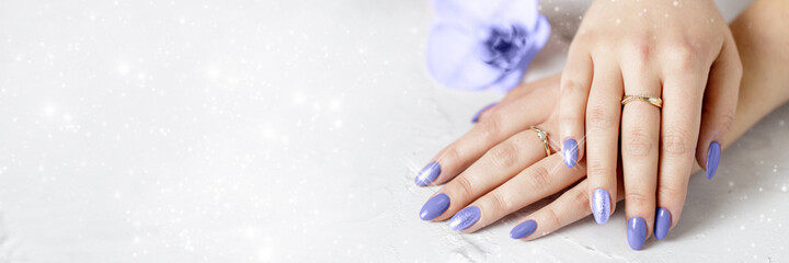 Beautiful hands with fresh violet manicure holding orchid flower and lying on a white. Spa or wellness holiday winter banner. Trendy color 2022 Very Peri manicure