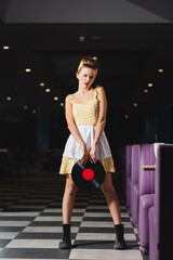 pin up woman in dress frowning while holding vinyl record disc.