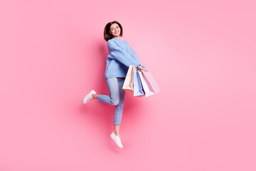 Full length body size view of attractive cheery cute girl jumping carrying bags isolated over pink pastel color background