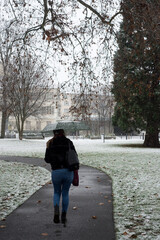 Portrait on back view of woman walking in a public garden with umbrella by snowy day