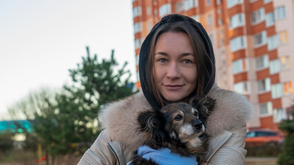 Beautiful girl hugs cute little dog after visits vet. A girl walks on the street with a small dog after surgery.