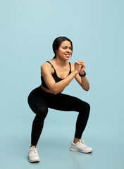 Fototapeta na wymiar Fitness and sport concpet. Fit black lady in sportswear doing deep squat exercise during workout on blue background