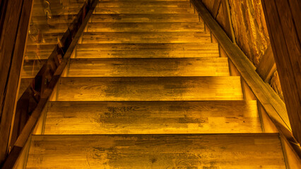 Yellow led light pouring from below onto a wooden staircase. Space for text. Abstract background.