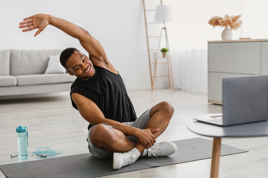 African American Guy Doing Stretching Exercise At Laptop At Home - Powered by Adobe