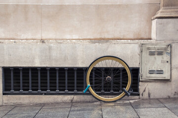 One wheel of a bicycle chained by two locks to the facade of the house, the concept of the problem of theft of bicycles in the city - 474222479
