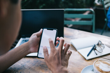 Cropped image of male blogger holding modern cellphone device and typing text during online messaging with social followers, millennial guy connecting to 4g internet for sending sms via cellular app